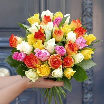 Buquê colorido de rosas segurado à frente de uma porta escura