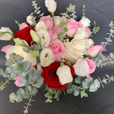 Buquê de rosas vermelhas, brancas e cor de rosa com folhas de eucalipto verde prateado sobre fundo cinza escuro
