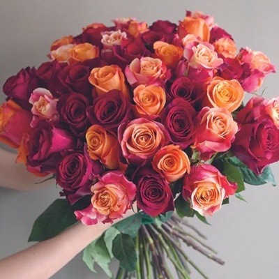 Buquê de rosas multicoloridas sendo segurado por duas mãos