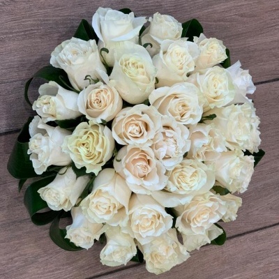 Bouquet redondo de rosas brancas com folhas verdes sobre superfície de madeira