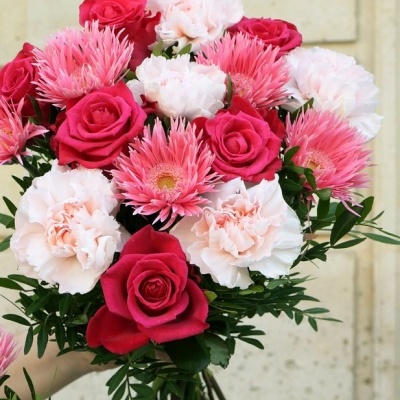Ramo de flores com rosas vermelhas, cravos cor-de-rosa e folhagem verde, mãos segurando