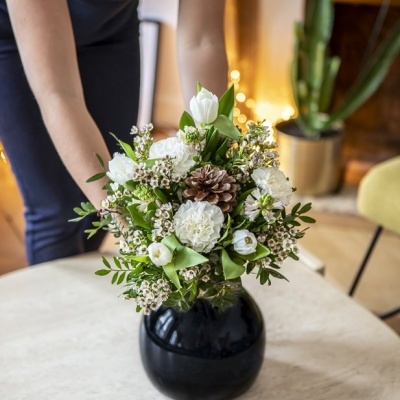 Vaso preto com arranjo floral branco e verde numa mesa branca interior