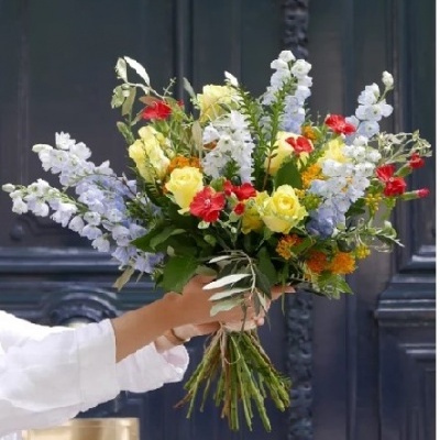 Buquê de flores coloridas segurado por pessoa em frente a porta azul