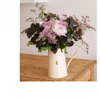 Jarro branco com flores rosas e lilases sobre mesa de madeira