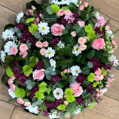 Arranjo circular de flores coloridas sobre chão de madeira