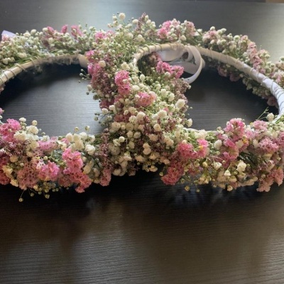 Duas coroas de flores artificiais ou secas em tons rosa, branco e verde sobre madeira escura