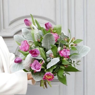 Bouquet de flores rosas com folhas verdes e cinzentas segurado por pessoa com roupa branca