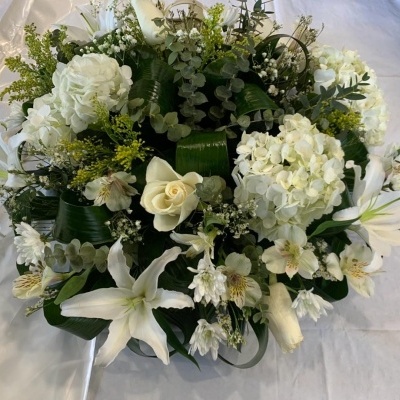 Arranjo floral com flores brancas e folhas verdes sobre tecido branco