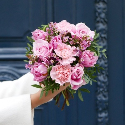 Buquê de flores rosas com folhagem verde segurado em frente a porta azul