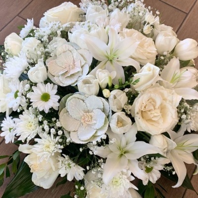 Arranjo floral branco com várias flores sobre chão de madeira.