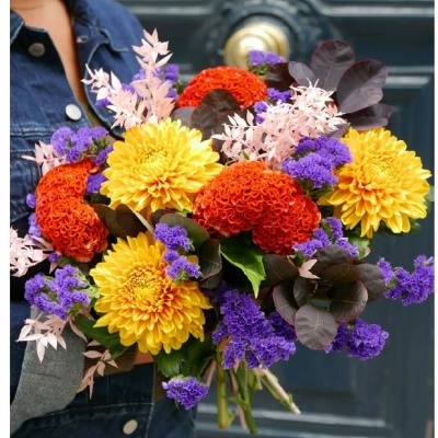 Ramo colorido de flores variadas segurado em frente a uma porta azul