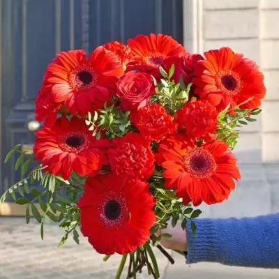 Bouquet de flores vermelhas com folhas verdes segurado por mão com suéter azul