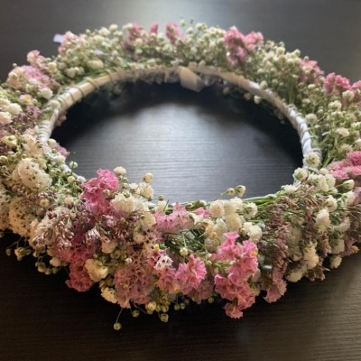 Coroa floral com flores pequenas secas em branco e rosa sobre superfície escura