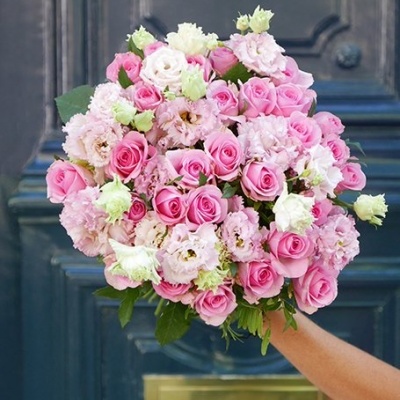 Buquê de rosas cor-de-rosa e flores brancas segurado em frente a uma porta azul escura