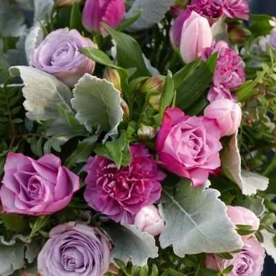 Arranjo floral com rosas e cravos em tons de rosa e lilás com folhas verdes e cinzentas