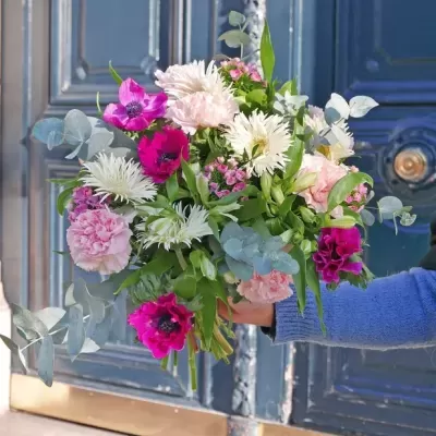 Ramo de flores várias cores com folhagem segurado junto a uma porta azul