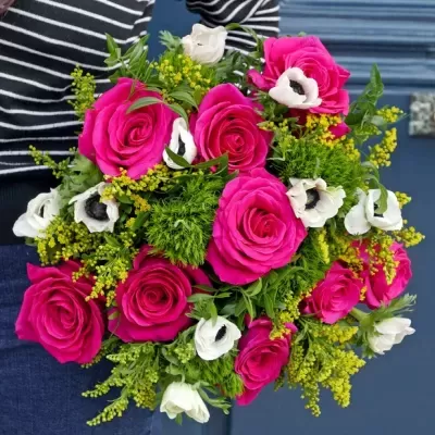 Buquê de rosas laranja, flores brancas e folhagem verde segurado por pessoa com camisa listrada.