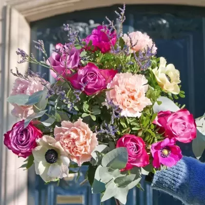 Bouquet colorido de flores diversificadas segurado junto a uma porta azul.