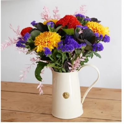 Ramo colorido de flores naturais num jarro branco em mesa de madeira