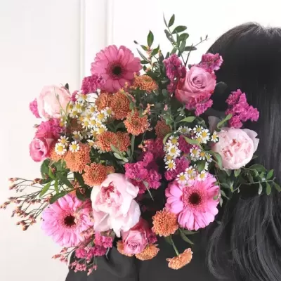 Ramo colorido de flores com tons de rosa, laranja e branco, sobre o ombro de uma pessoa de cabelo preto.