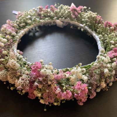Coroa de flores pequenas em tons de branco e rosa sobre superfície escura