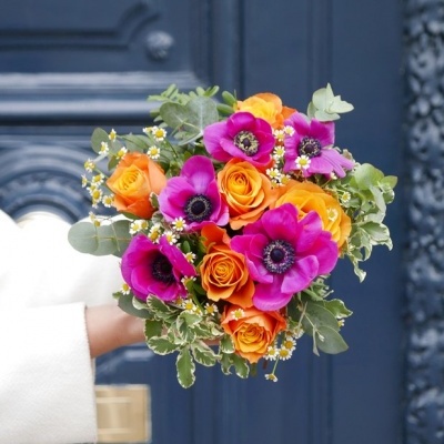 Buquê colorido de flores com rosas laranja e anémonas roxas em frente a porta azul