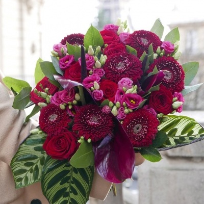 Buquê de flores vermelhas e roxas com folhas verdes em ambiente urbano desfocado