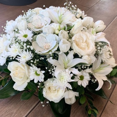 Arranjo floral com flores brancas variadas e folhas verdes sobre madeira.