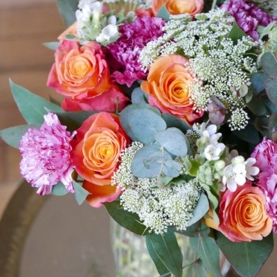 Buquê colorido em vaso de vidro com rosas e cravos, folhas verdes e flores brancas