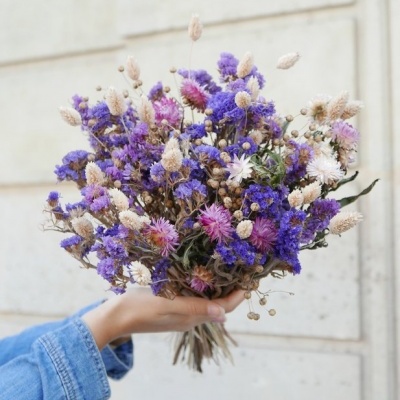 Ramo de flores secas multicoloridas segurado por mão com camisa azul de ganga
