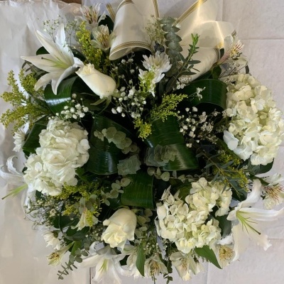 Arranjo floral redondo com flores brancas e folhas verdes escuras