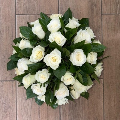 Arranjo redondo de rosas brancas com folhas verdes sobre chão de madeira clara