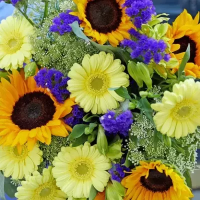 Ramo colorido de flores com girassóis, flores amarelas e roxas num vaso transparente