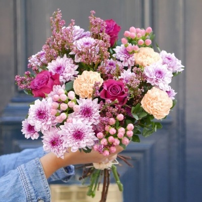 Buquê colorido de flores variadas segurado por mão com camisa de ganga