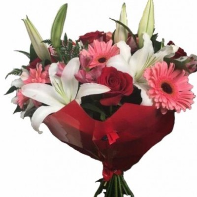 Buquê de flores com rosas vermelhas, lírios brancos e gerbera cor-de-rosa envolvido em papel vermelho