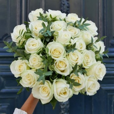 Ramo de 25 rosas brancas com folhas verdes seguidas por mão em fundo de porta azul escura