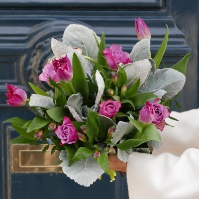 Bouquet de flores com rosas e tulipas cor-de-rosa e folhas verdes e cinzentas na frente de uma porta azul escura