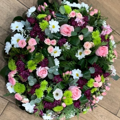 Arranjo floral circular com flores brancas, rosas, verdes e roxas sobre piso de madeira