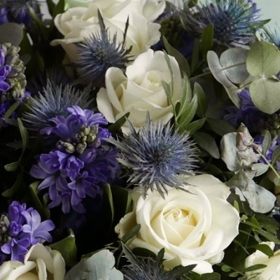 Bouquet de rosas brancas, flores roxas e azuis e folhagens secas num fundo neutro