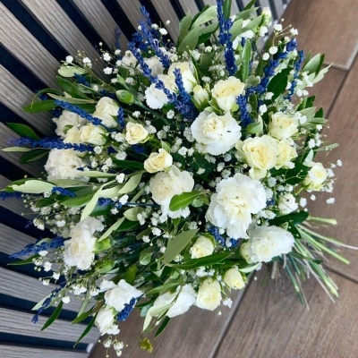 Bouquet de flores brancas e azuis com folhagem verde em banco de madeira.