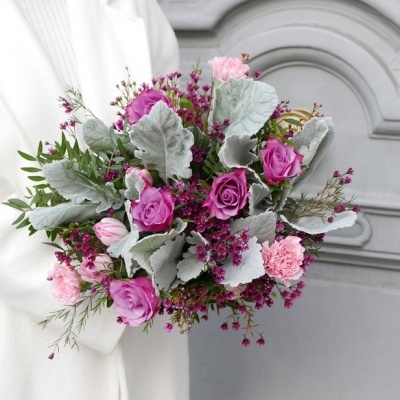 Buquê de flores rosas com folhas cinza-esverdeadas segurado em casaco branco