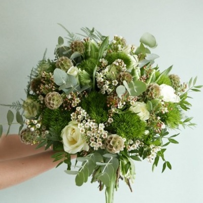 Bouquet de flores brancas e verdes com folhagens variadas num fundo cinzento claro