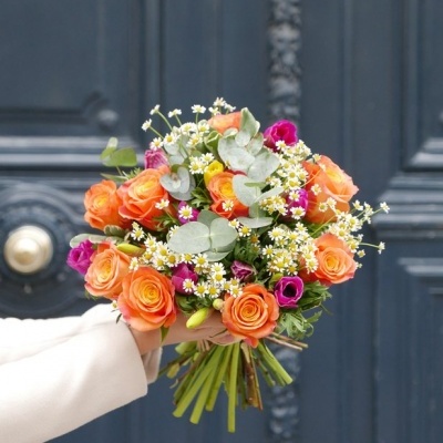 Ramo de flores coloridas com rosas laranja e flores pequenas em frente a porta azul