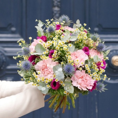 Ramo de flores coloridas com cravos e folhagem, segurado em frente a porta azul