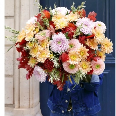 Bouquet de flores multicolores com folhas decorativas segurado por pessoa com casaco de ganga azul