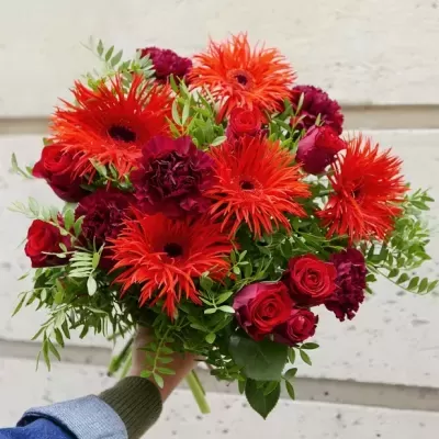 Bouquet de flores vermelhas e laranjas com folhagem verde segurado por uma mão