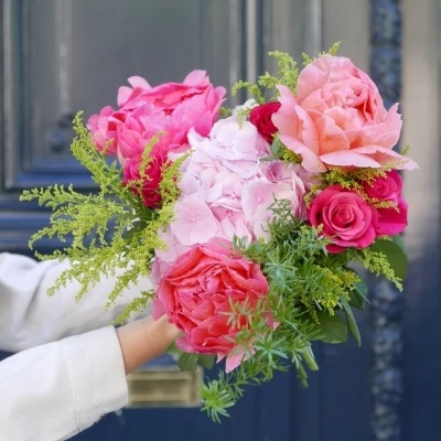 Ramo colorido de flores segurado por mãos à frente de porta azul