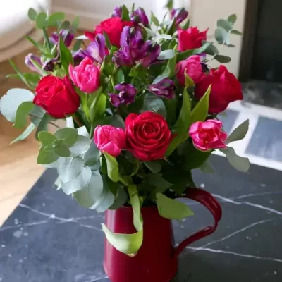 Buquê de flores coloridas em jarro vermelho sobre mesa escura