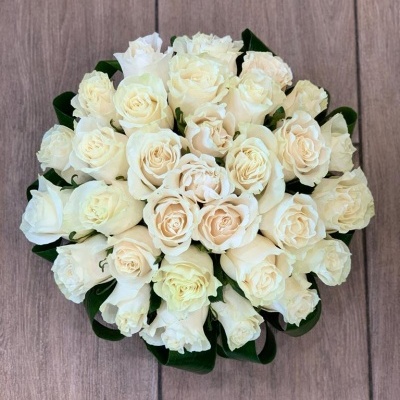 Arranjo de rosas brancas com folhas verdes em piso de madeira