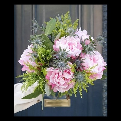 Bouquet de peónias cor-de-rosa com folhagem verde e flores espinhosas cinza-azuladas